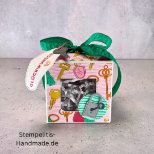 handdekorierte Fensterschachtel mit Glückwunsch-Anhänger, Geschenkbox mit Schlüsselmotiv und grünem Band, Nahaufnahme Fenster der Schachtel mit Füllung, runder Anhänger mit Schloss und Schlüssel, Schachtel geöffnet mit sichtbarem Inhalt, Glückwunsch-Tag an Geschenkbox, Geschenkverpackung für Einzug oder Prüfung